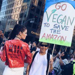 miss montana next to a sign at a rally that says go vegan