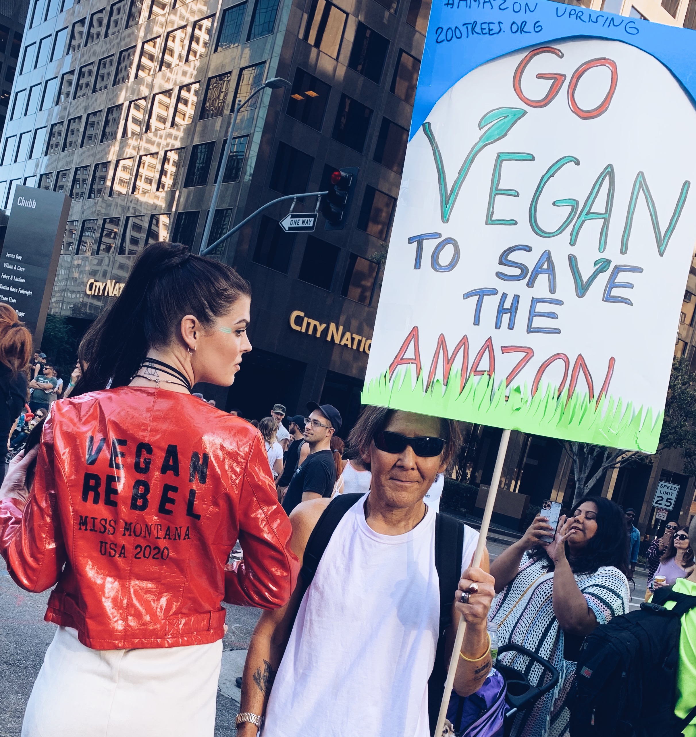 miss montana next to a sign at a rally that says go vegan