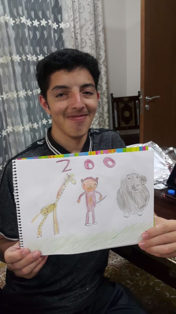 student holding a drawing of a zoo with three animals