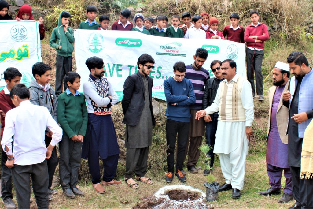 Man wearing white giving demo to group of students about how to plant a tree