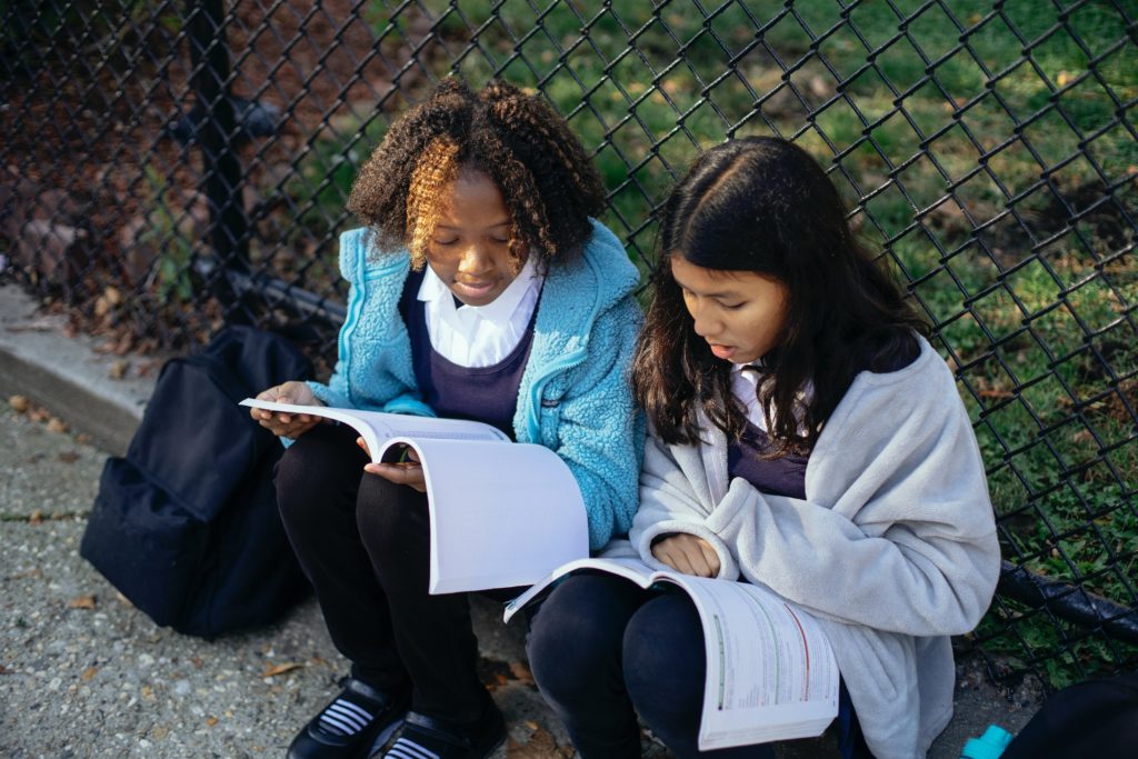 Two children doing homework next to a fence outside