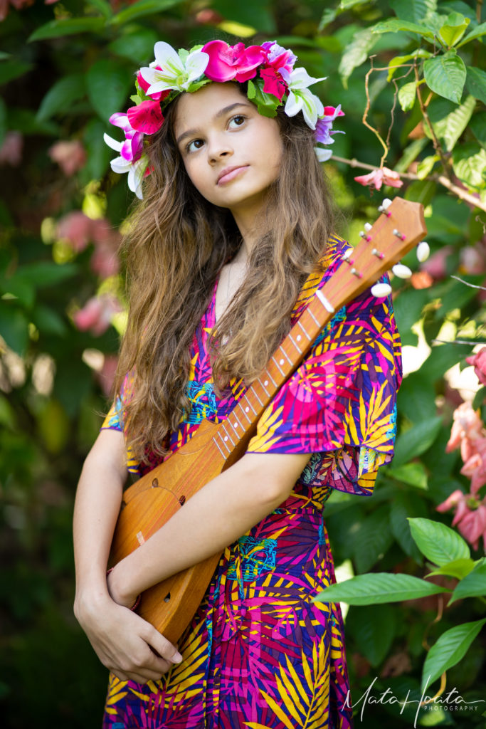 Girl holding a guitar-like instrument and with pink and white flowers on her head