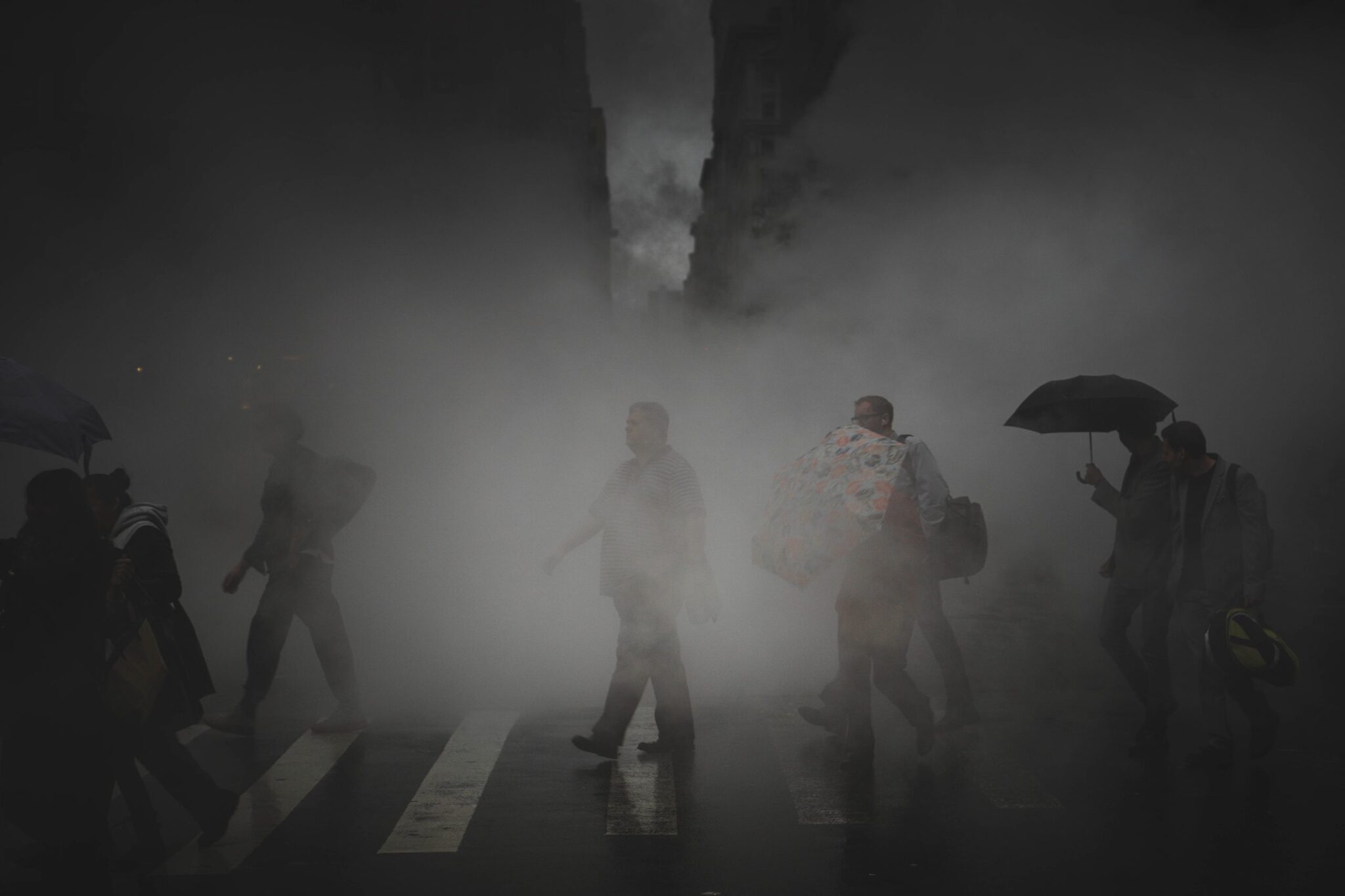 pedestrians walk on a crosswalk and through steam