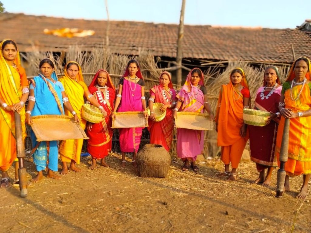 10 women in yellow, bue, red, orange, and pink clothing holding handmade bowls and plates