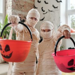 Two people dressed up as mummies and holding orange pumpkin baskets