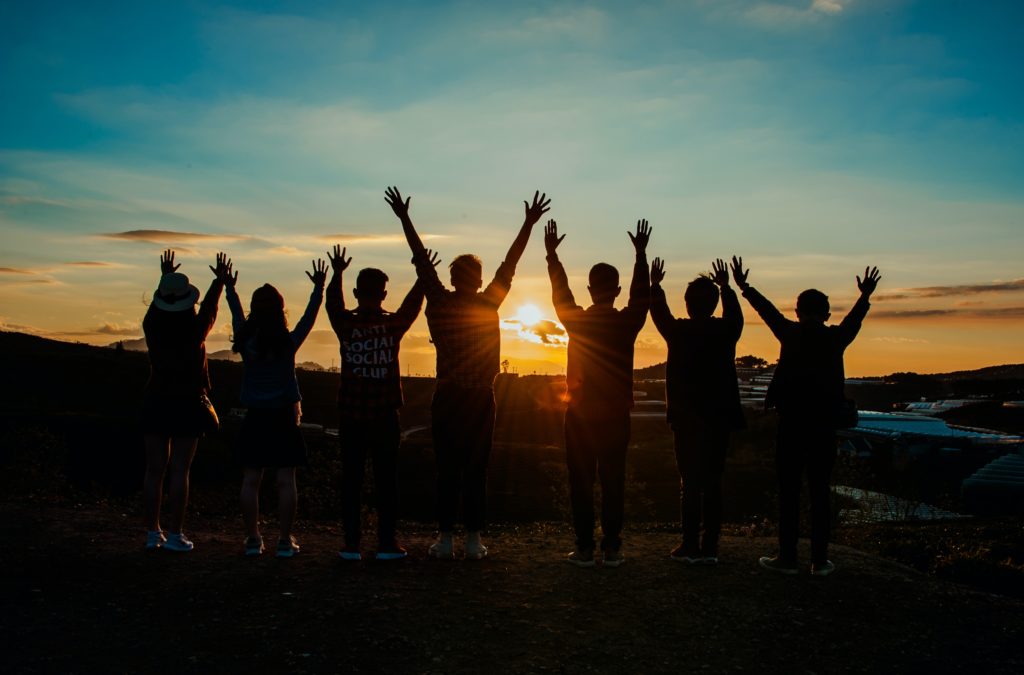 Group of people cheering from behind in front of a sunset