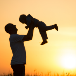Father holding a child in front of a sunset.