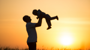 Father holding a child in front of a sunset.