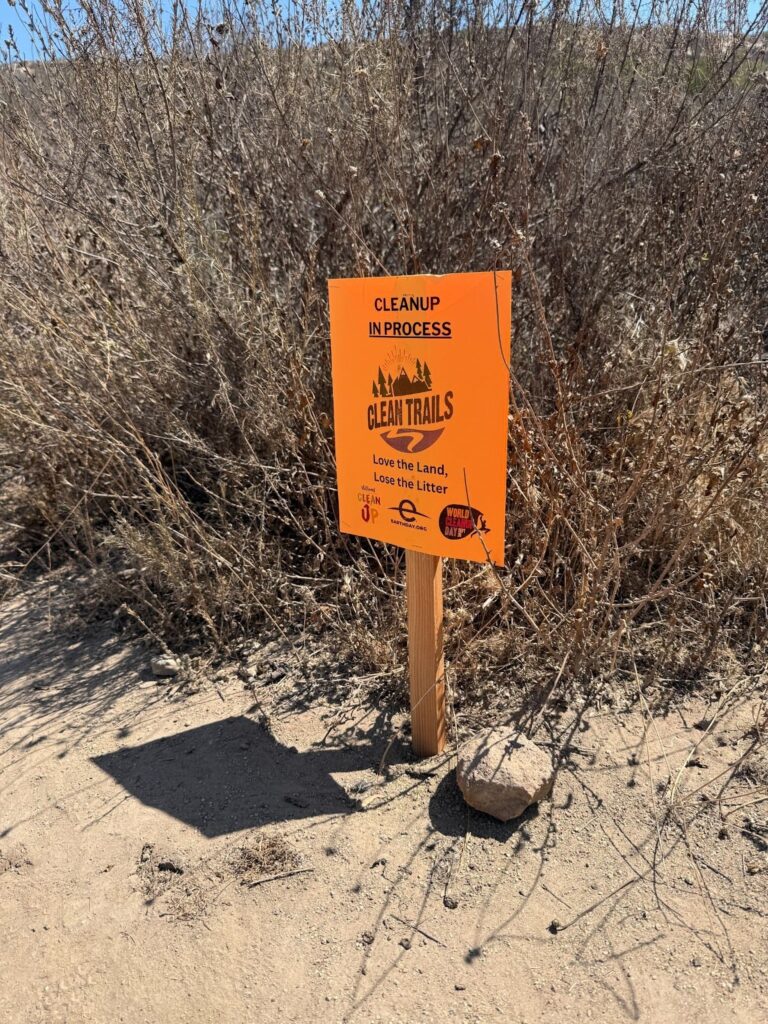 Orange sign with black type "Cleanup in Progress," Clean Trails logo," Love the Land, Lose the Litter tagline