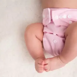 A baby lays on a bed wearing a cloth diaper. Aurora Uribe