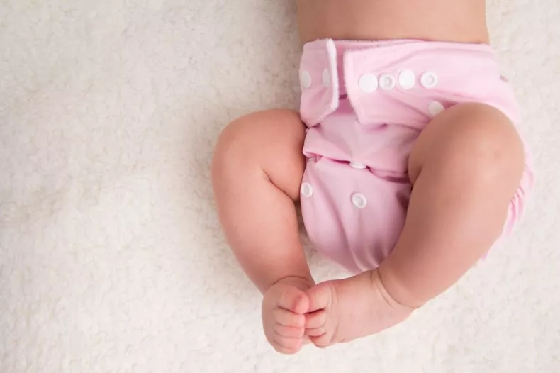 A baby lays on a bed wearing a cloth diaper. Aurora Uribe