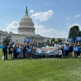 Coalition of many members standing outside the Capital, with signs and a banner