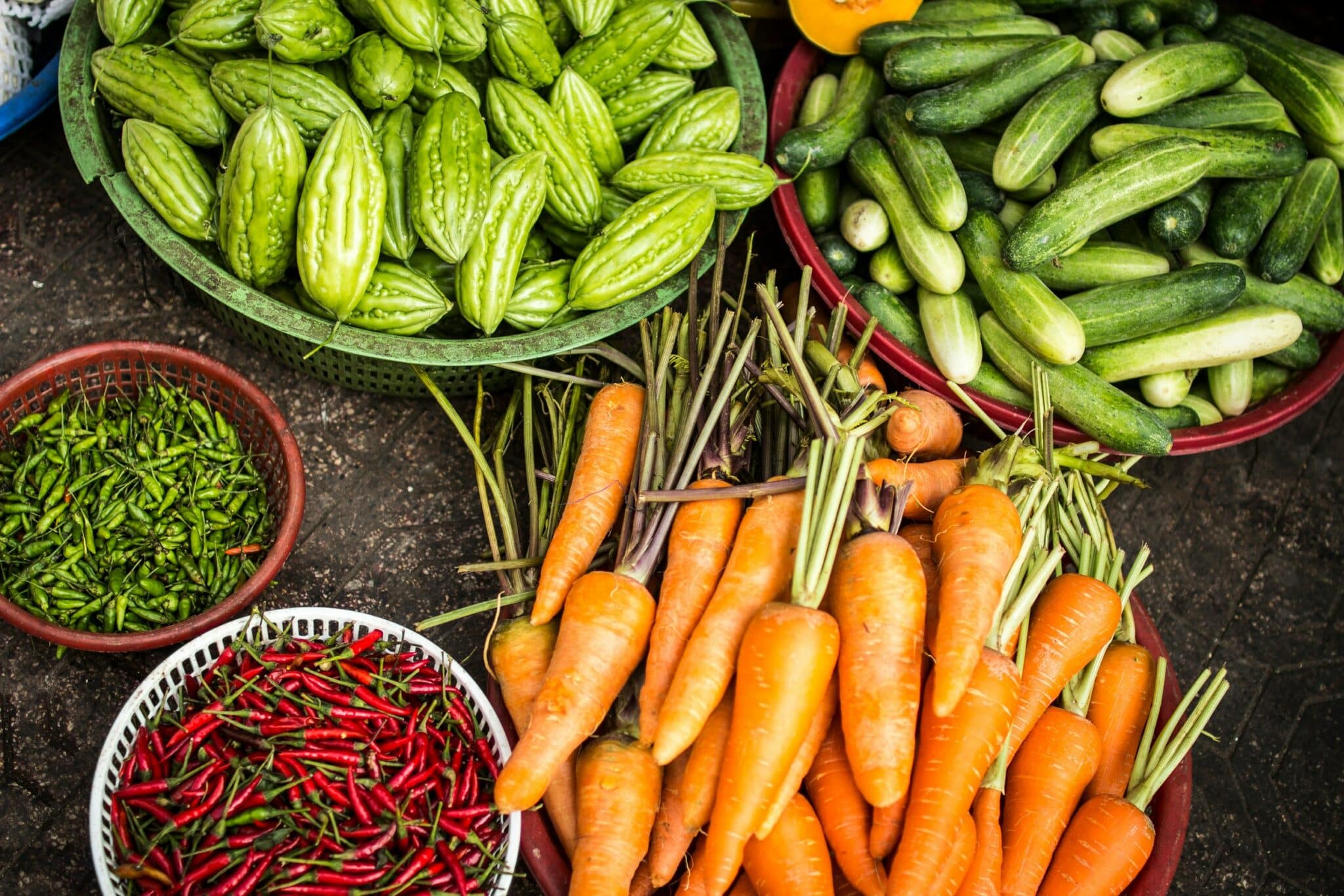 Baskets of fresh carrots, cucumbers, bitter melon and chili peppers at a market
